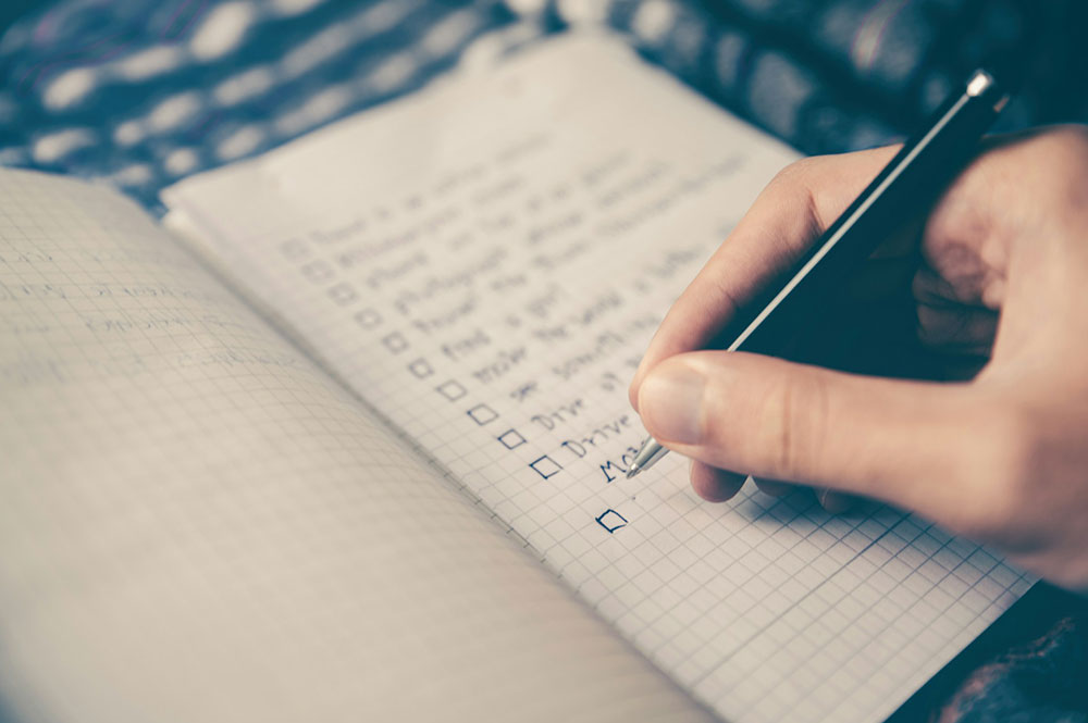 Someone holding a pen writing a checklist in a notebook