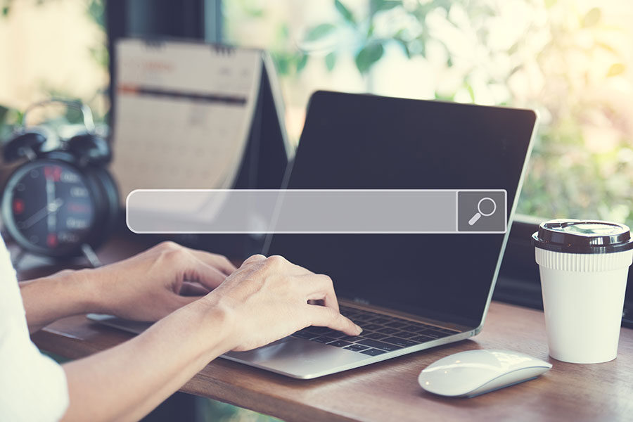 A person sat at a laptop with a search bar overlapped on the image to represent Search Engine Optimisation